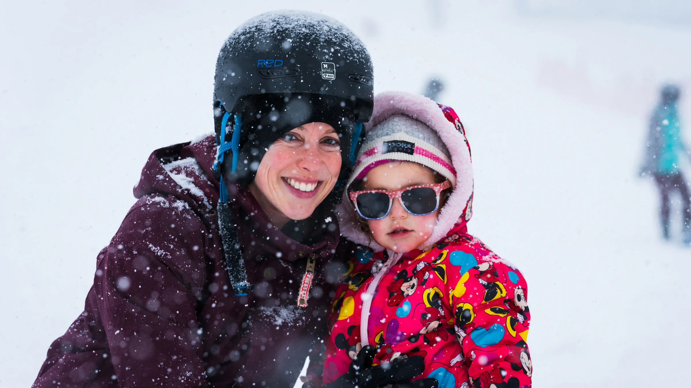 Adult with their child smiling at the camera during a snow storm